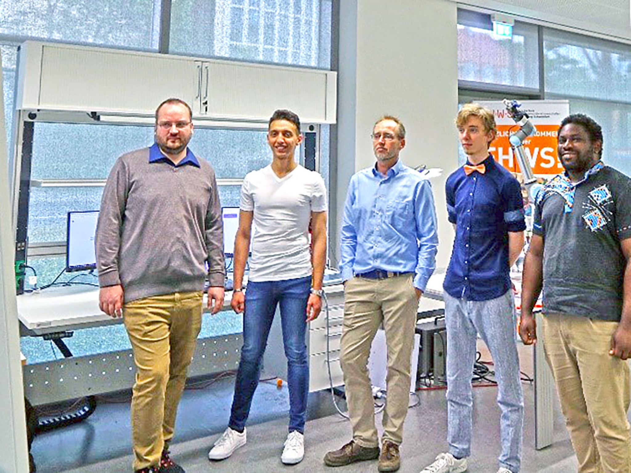 FHWS_Teamfoto Wettbewerb Das Team „RoboPig“ um Prof. Dr. Tobias Kaupp (Mitte) verfolgt gespannt den Livestream der Award Show. Im Hintergrund ist der Roboterarm zu sehen, mit dem das Team die Aufgabenstellung löste. Foto: Fabian Dax