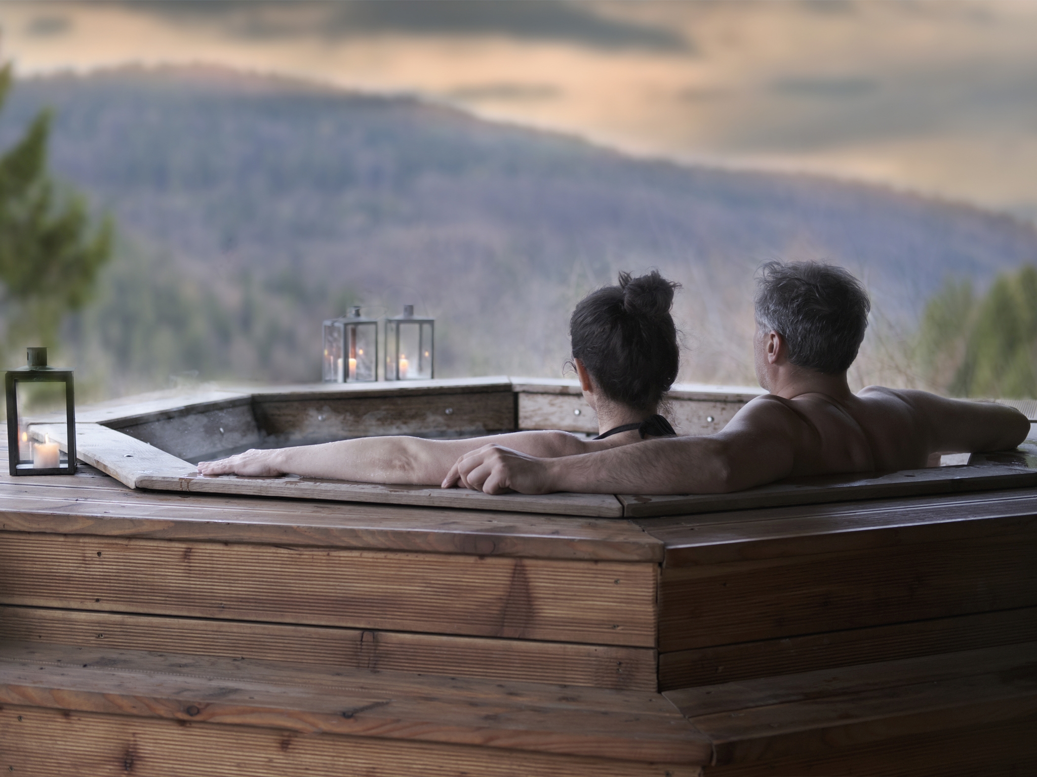 The young couple in an open-air bath with a view of the mountains. Nach der Wanderung im Whirlpool ausspannen. So schön kann Ihre Perspektive für das Jahresende 2022 aussehen. Foto: Getty Images