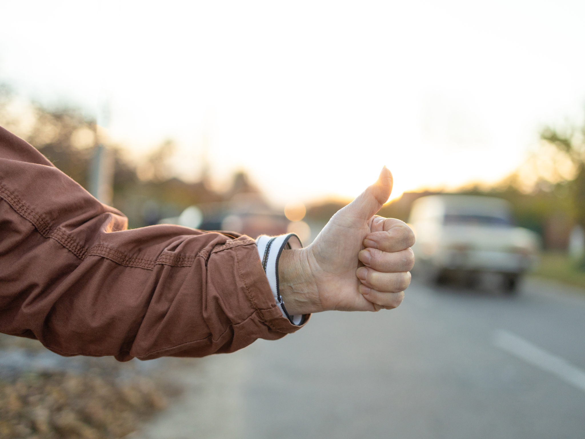 Female hand and hitchhiking sign on road, traveling by autostop in the city. Woman try stop car thumb up. Adventure and tourism concept